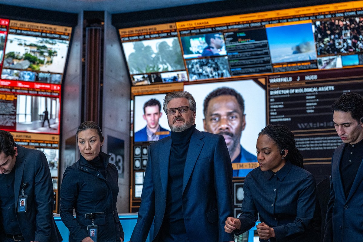 Noah Scanlon played by Colin Firth standing in the high-tech WARDEX tactical operations control room with monitors tracking Daniel Kellner and Hugo Wakefield in Steven Spielberg's Disclosure Day 2026.