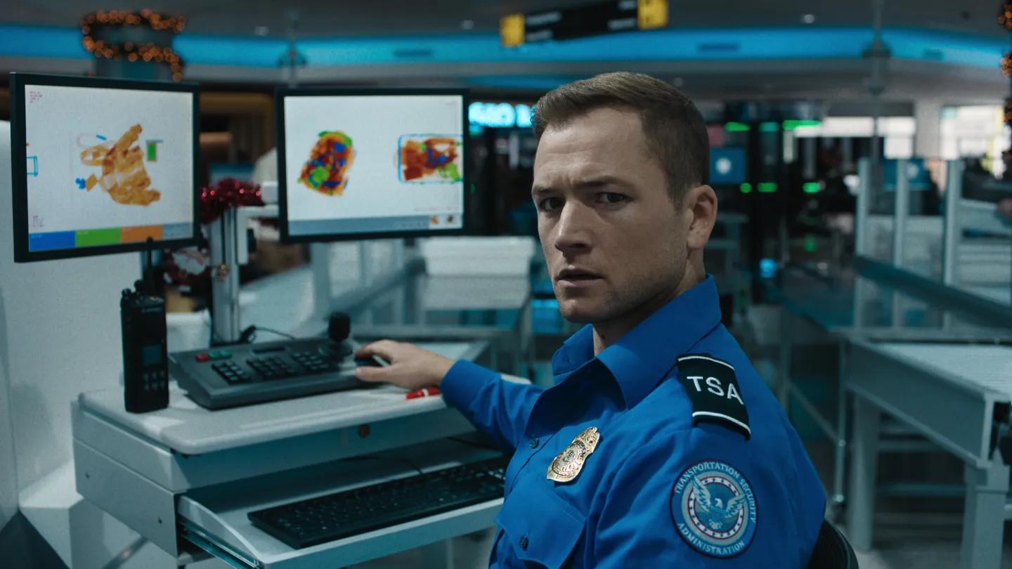 Taron Egerton in TSA uniform at an airport security scanning station in Carry-On