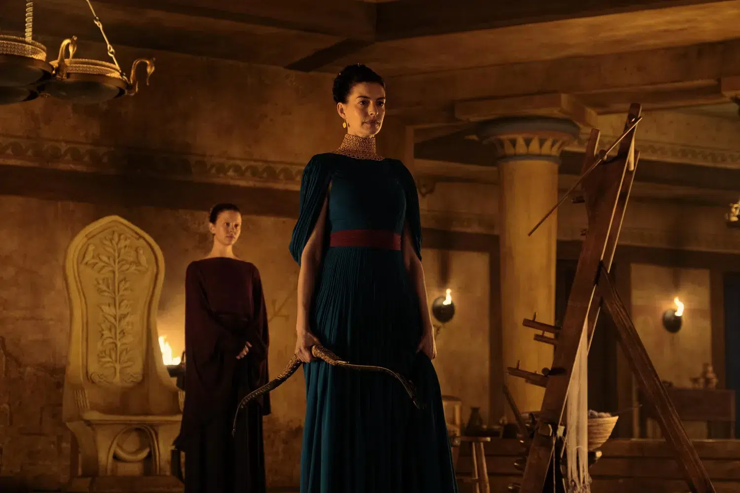 Anne Hathaway as Penelope holding Odysseus’s bow, with Mia Goth as Melantho behind her in Christopher Nolan’s The Odyssey.